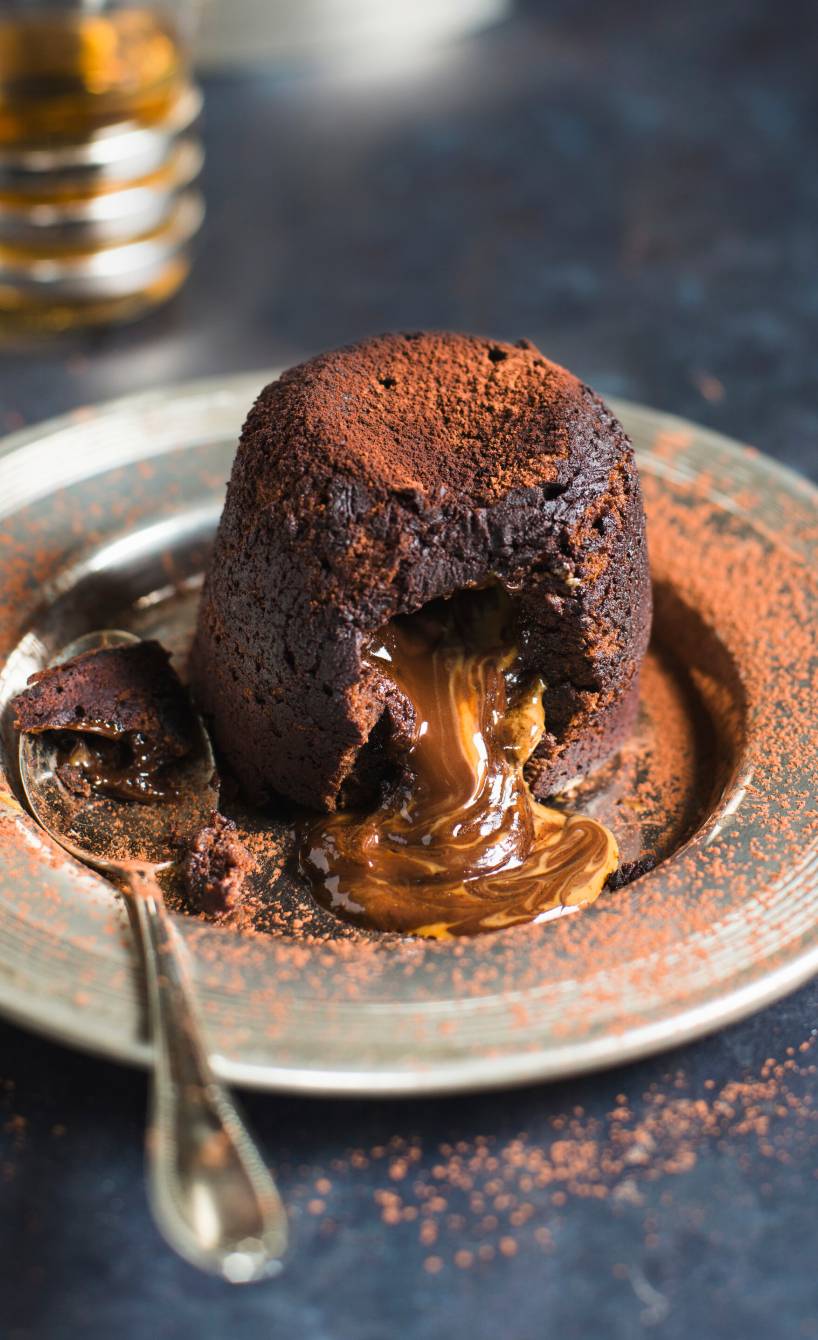 Halb geöffnetes Schoko-Lava-Küchlein auf einem Dessertteller mit herauslaufendem flüssigem Karamell