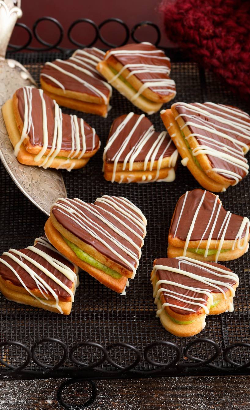 Doppeldeckerplätzchen in Herzform mit Pistazienfüllung und Schokolade auf einem Kuchengitter