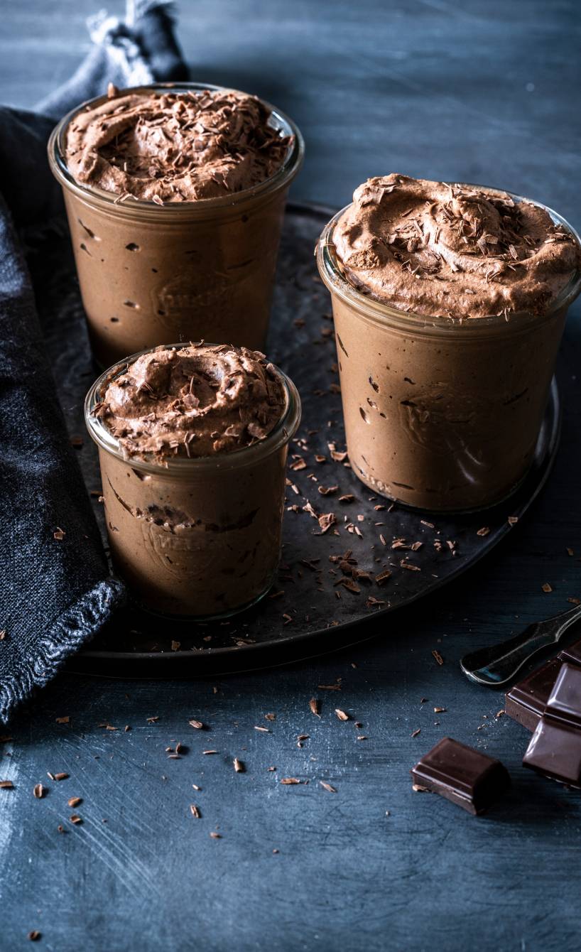  Schokomousse in drei Dessertgläser getoppt von geraspelter Schokolade auf einem festlich dekorierten Tisch