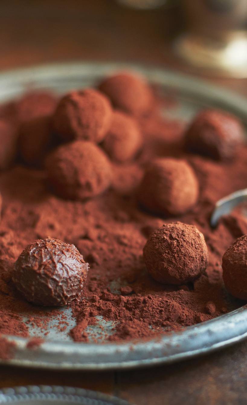 Schokotrüffel mit Zimt und Kakao bestäubt auf einem Tablett mit einer Zange