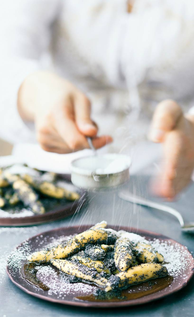 Selbstgemachte Schupfnudeln mit Mohnbutter auf einem Teller werden mit Puderzucker bestäubt