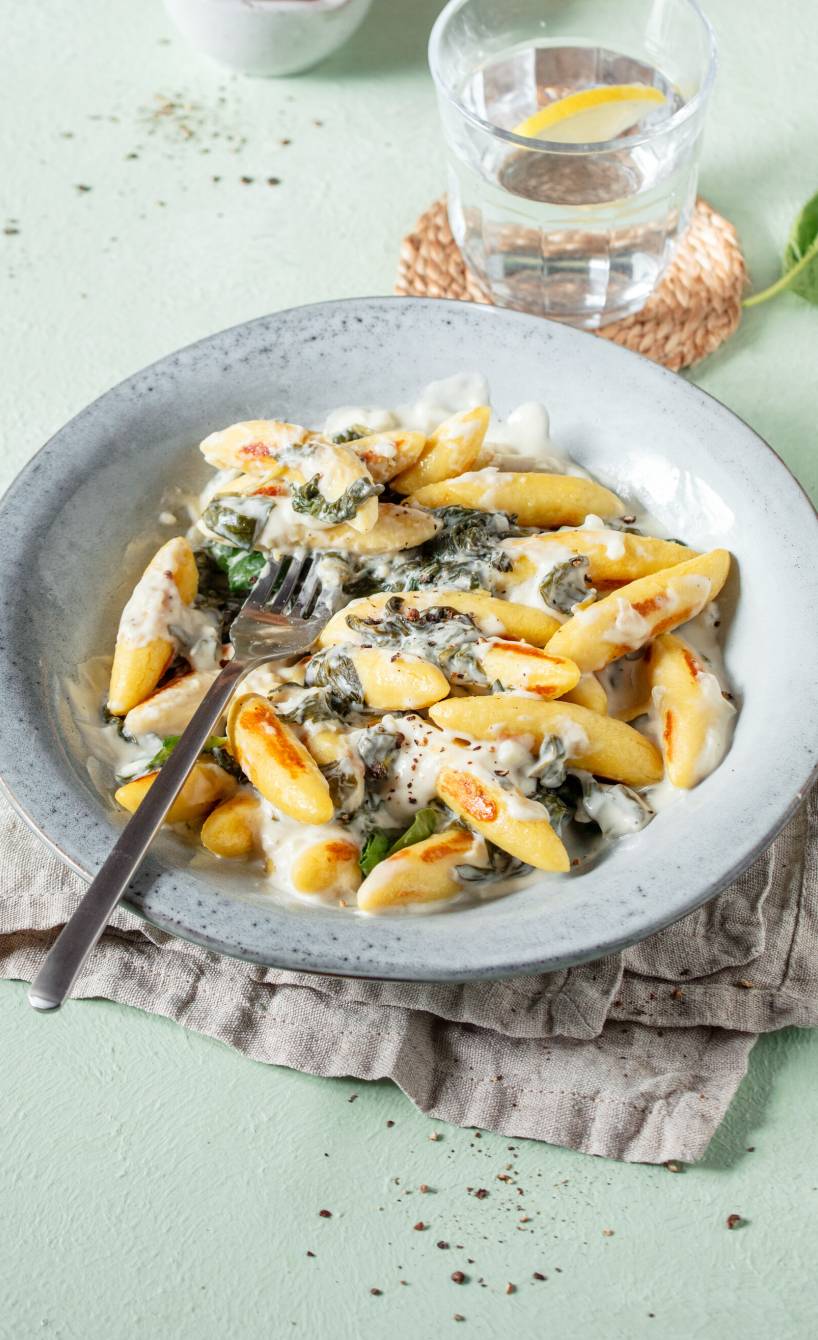 Schupfnudeln mit Spinat-Ricotta-Soße angerichtet auf einem tiefen Teller