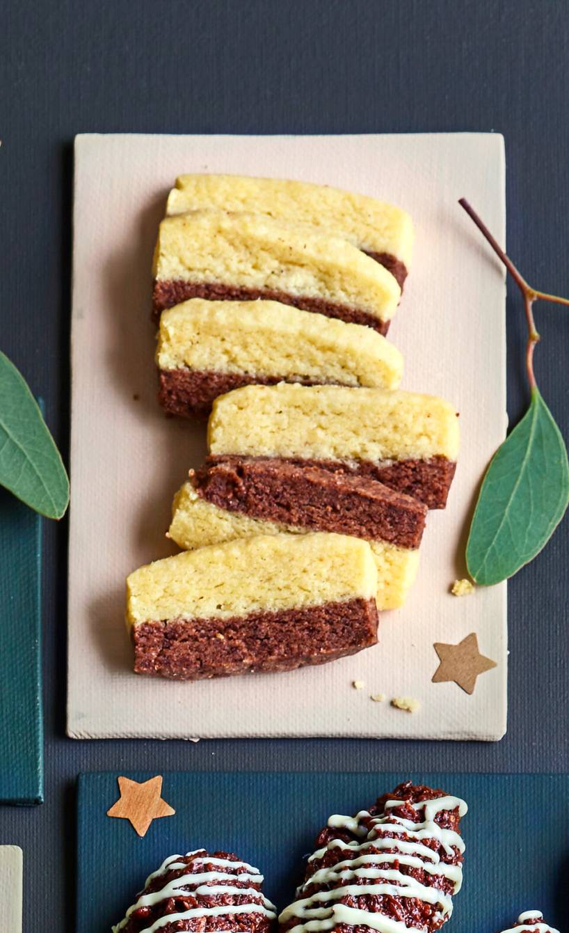 Schwarz-Weiß-Gebäck auf einem Marmorbrettchen, daneben Mistelzweige und andere Plätzchen