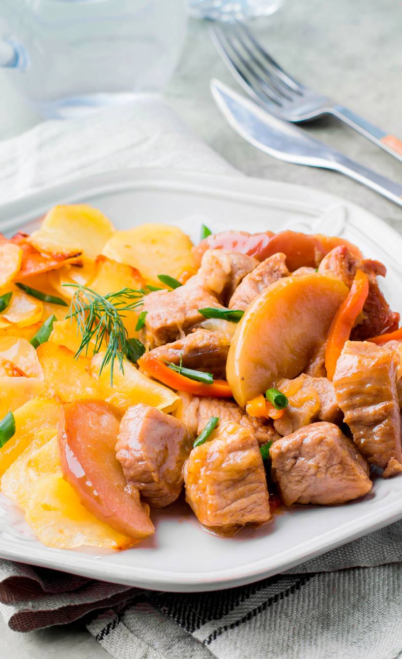 Schweinegulasch auf einem Teller mit Äpfeln und Kartoffelgratin
