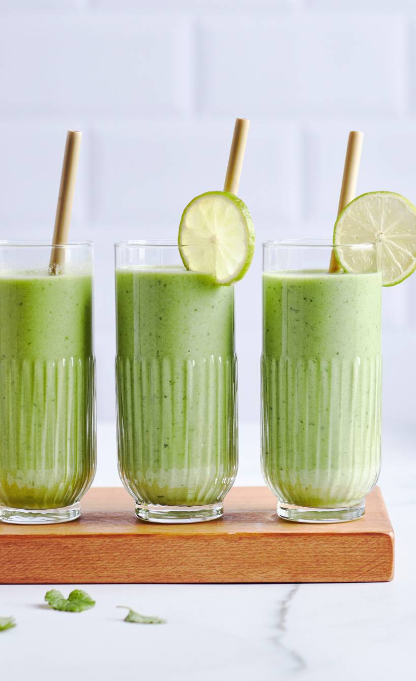 Grüner Smoothie in drei Gläsern auf einem Tisch mit Avocado, Gurke, Banane & Spinat