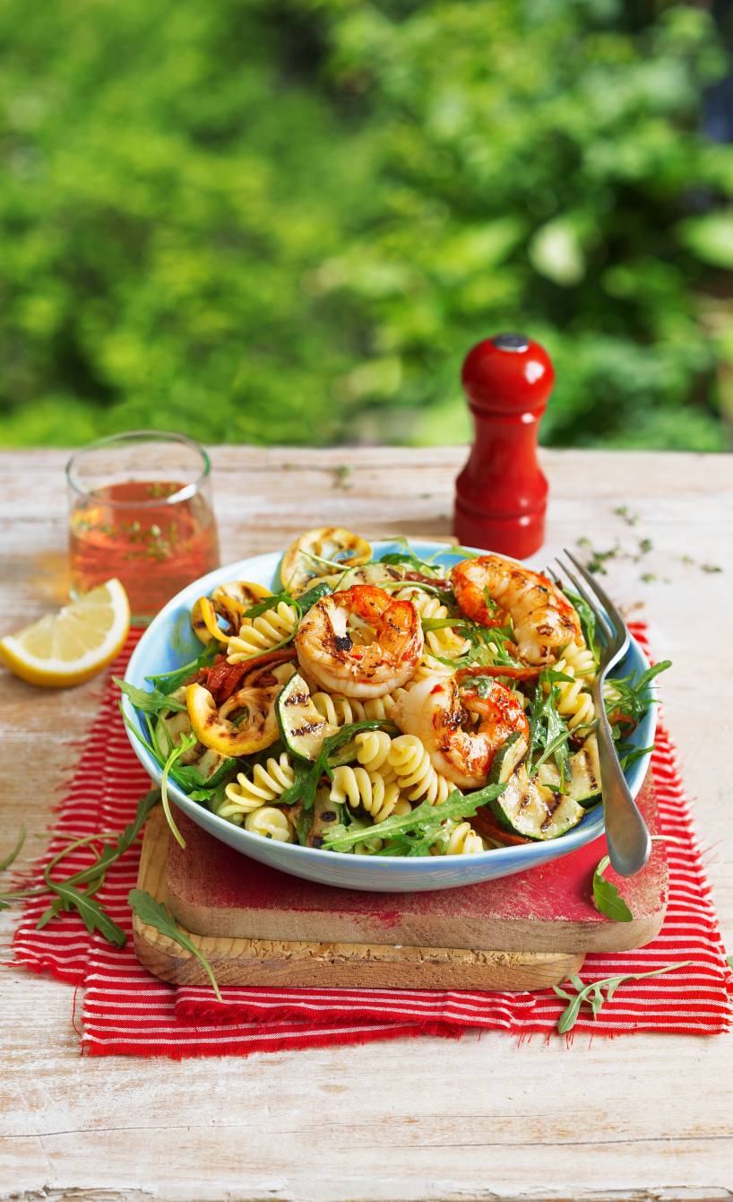 Nudelsalat mit gegrillter Zucchini und gegrillten Garnelen in einer Salatschüssel auf einem Tisch