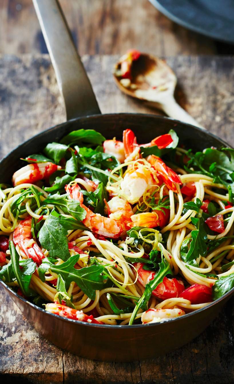 Spaghetti mit Garnelen, Rucola und Zitrone in einer gusseisernen Pfanne auf einem Holztisch