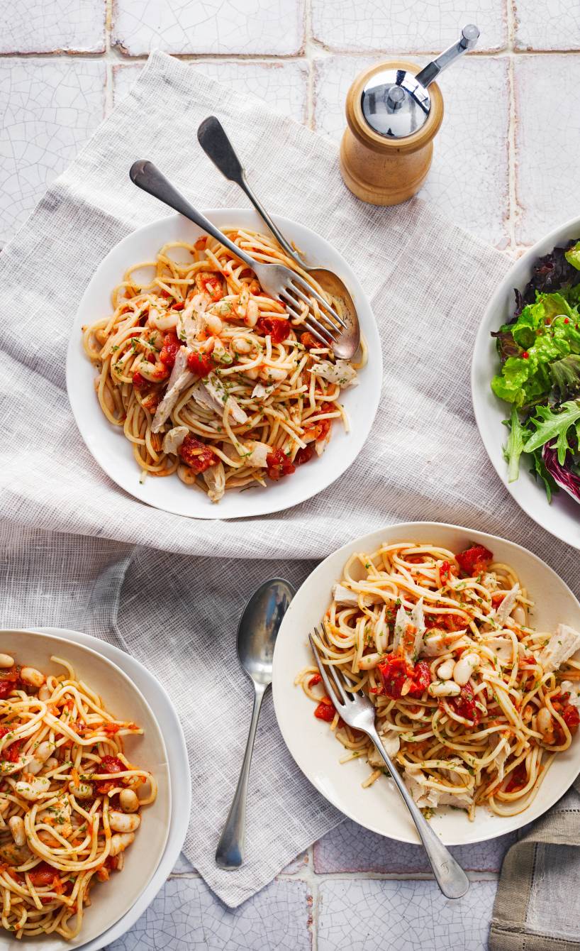 Drei Teller mit Thunfisch, Bohnen und frischen Kirschtomaten angerichtet auf einem Tisch, daneben eine Salatschüssel