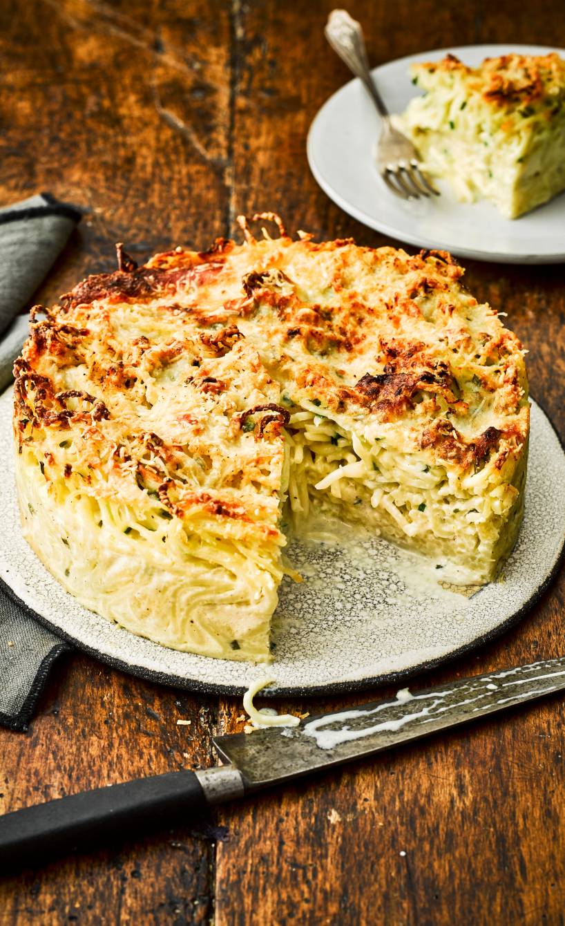 Runder Spaghettikuchen mit Sauce aus drei Käsesorten angeschnitten auf einem Teller