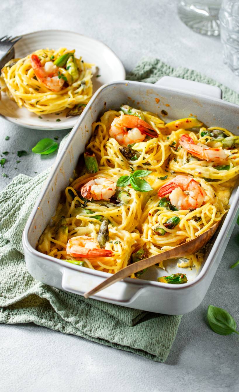 Auflaufform mit Sparhettinestern, grünen Spargelstücken und Garnelen auf einem Tisch