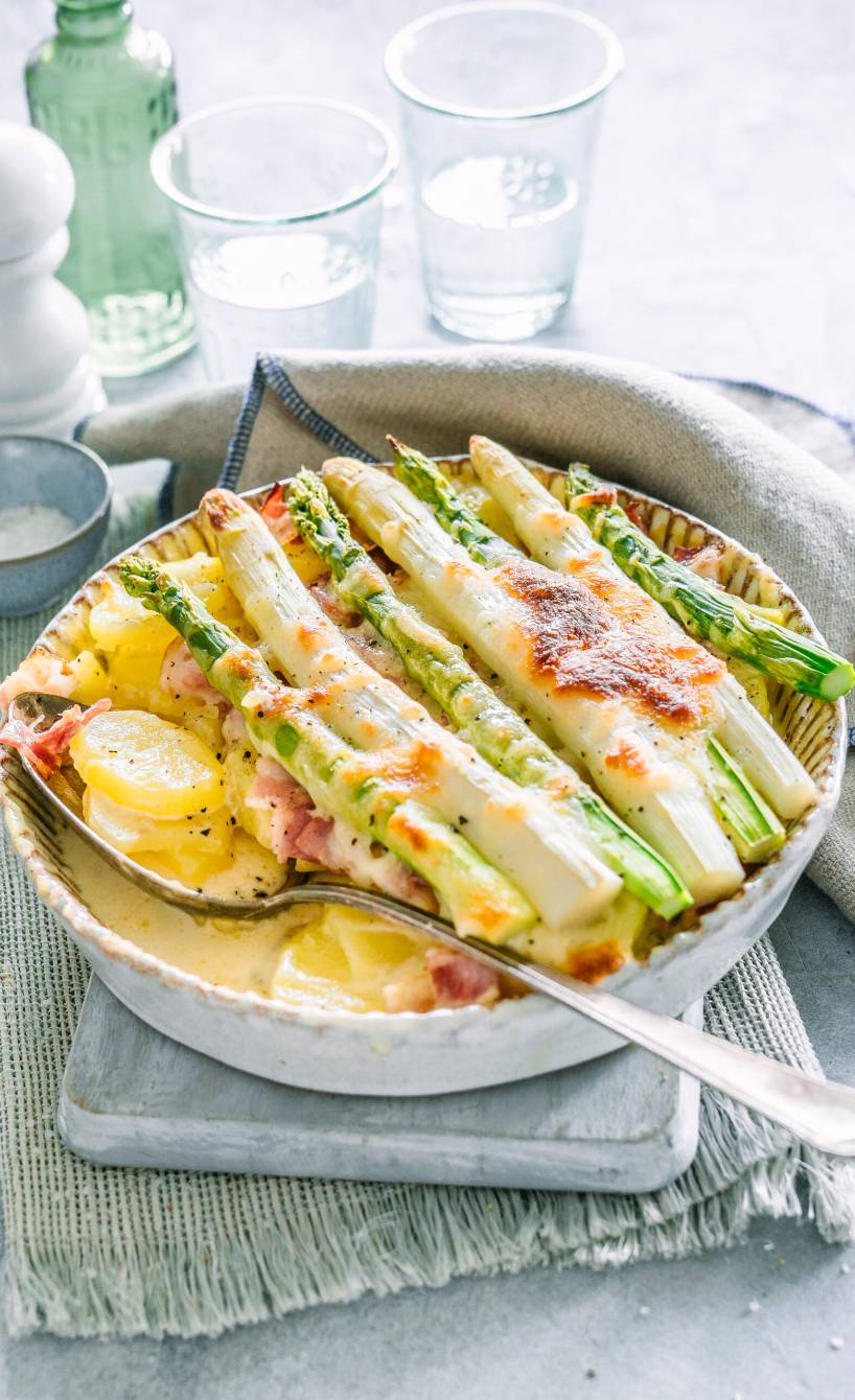 Kartoffelgratin mit Spargel, Schinken und Mozzarella in einer Auflaufform auf einem Tisch