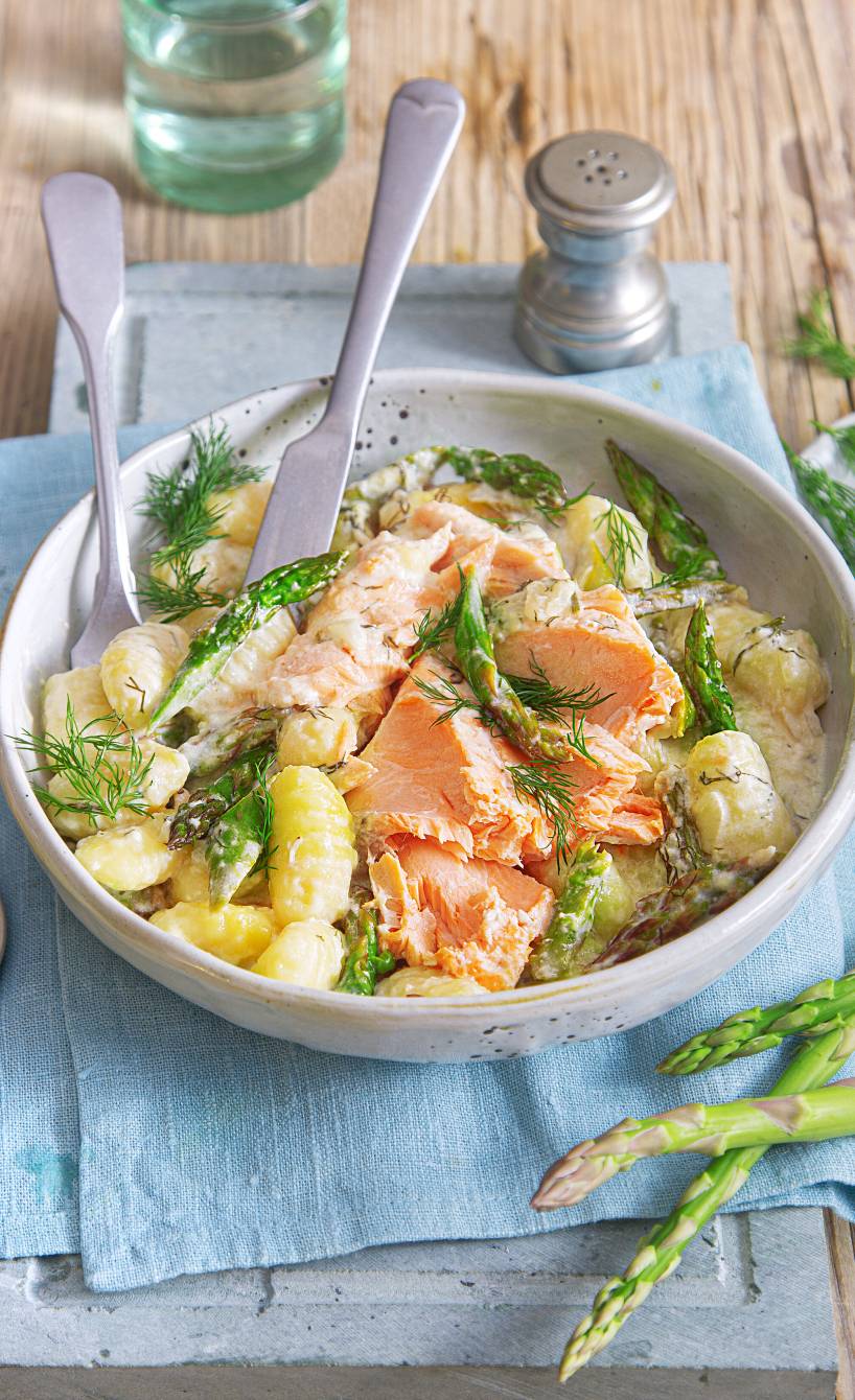 Auf dem Blech gebackene Gnocchi mit grünem Spargel und Lachsfilet in Sahnesauce auf einem tiefen Teller