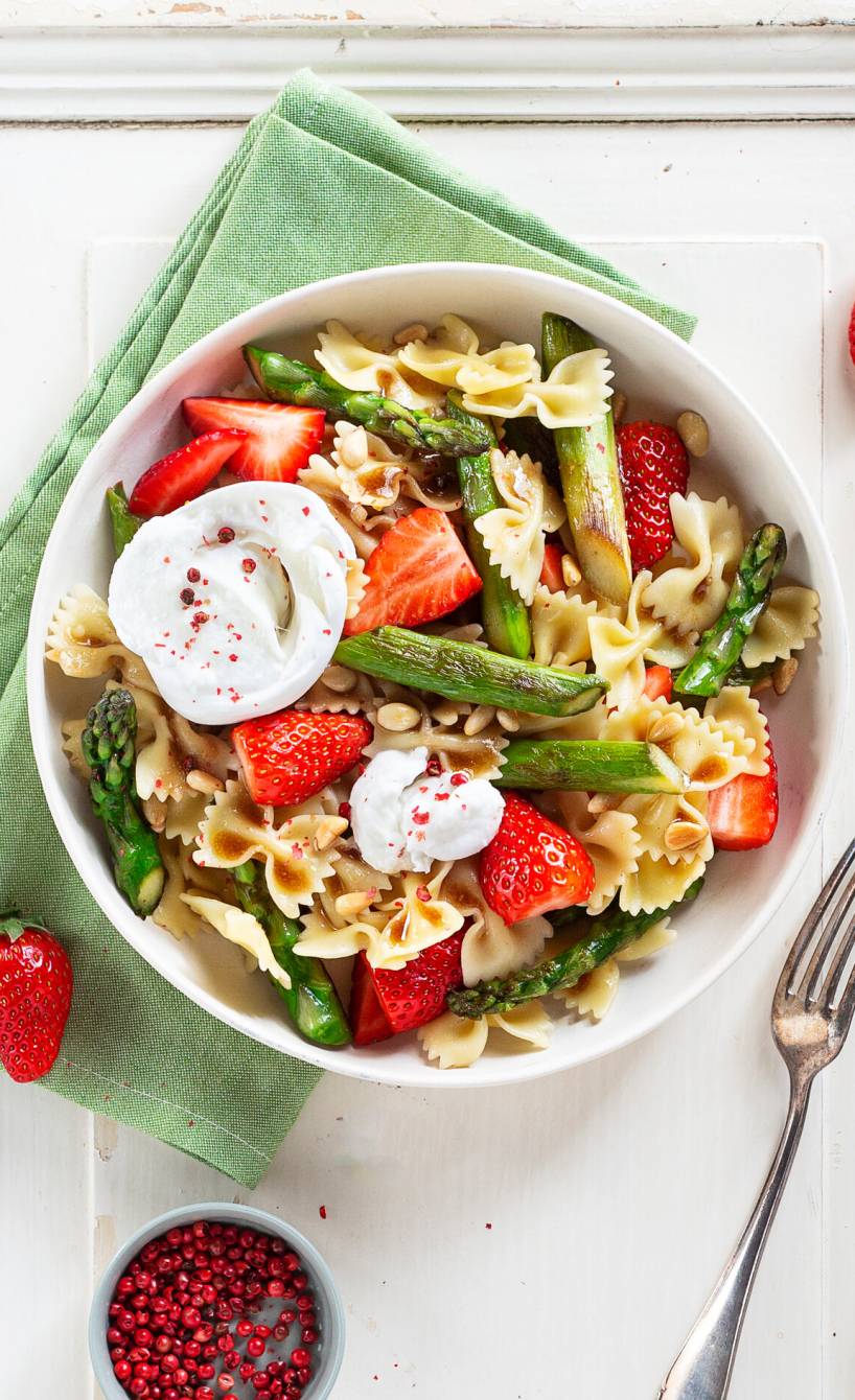 Spargelsalat mit Farfalle, Erdbeeren, Burrata und Pinienkernen in einer Schüssel auf einem Holztisch