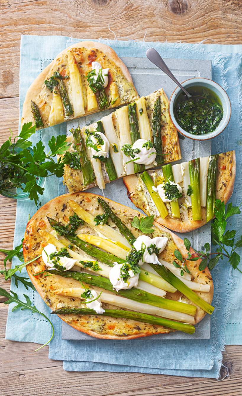 Spargelfladen aus Quark-Öl-Teig getoppt von Ziegenfrischkäse-Creme in Streifen geschnitten auf einem Holzbrett
