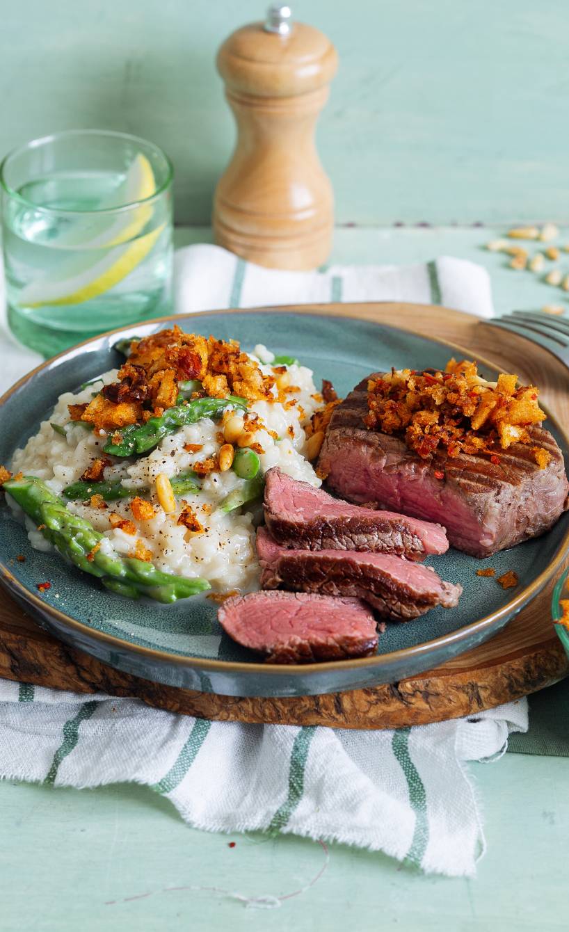 Spargelrisotto auf einem Teller, daneben Rindermedaillons aus dem Ofen getoppt mit Bröseln