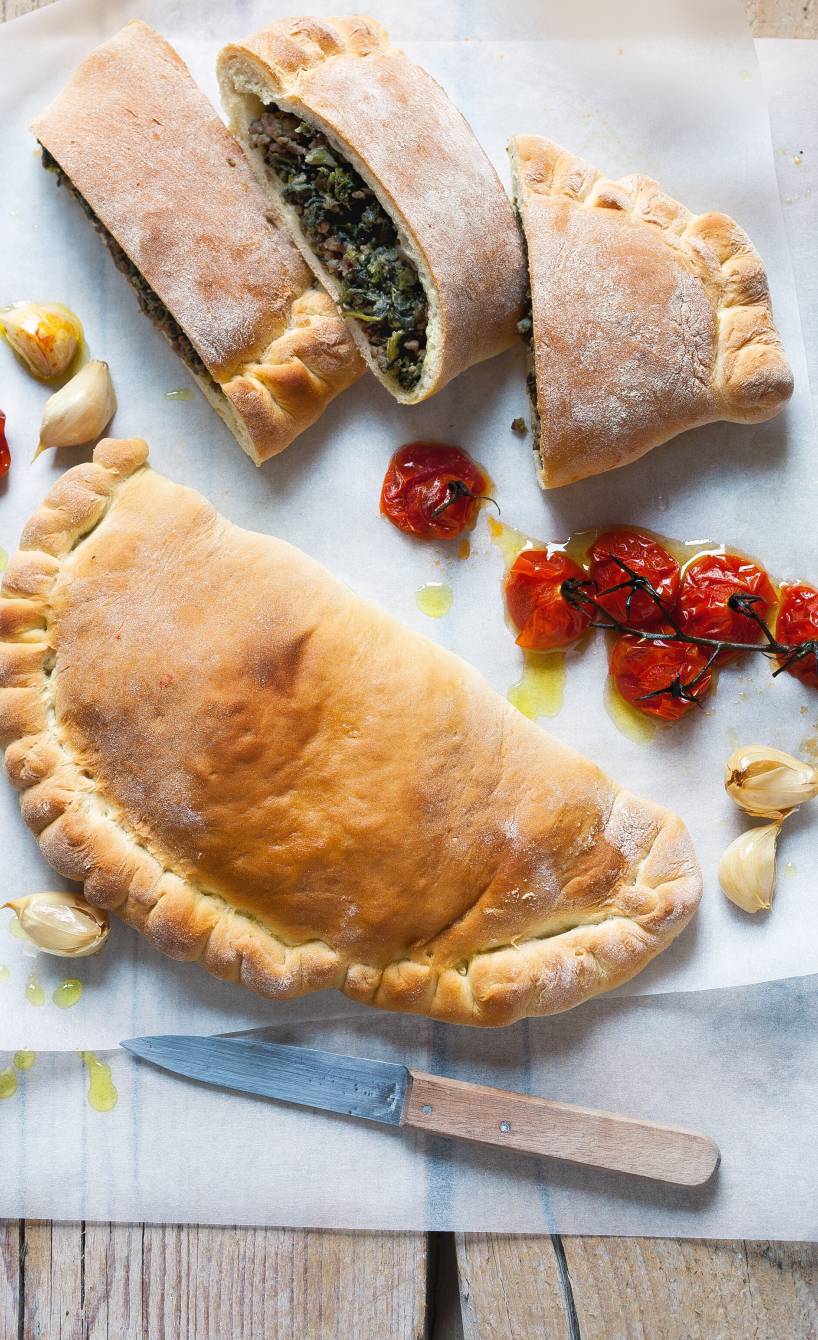 Zwei Calzoni auf einem Backpapier, davon eine aufgeschnitten mit Füllung aus Spinat, Ricotta & Hackfleisch