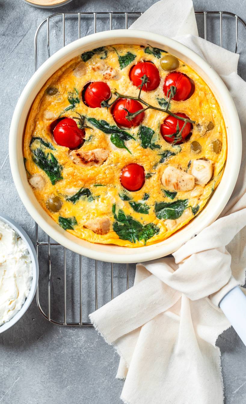 Frittata mit Hähnchen, Tomaten und Spinat in einer ofenfesten Pfanne, daneben Feta-Dip