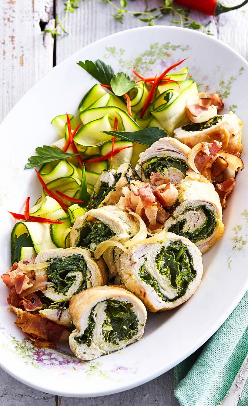 Puteninvoltini mit Spinatfüllung angerichtet neben Zucchinisalat, getoppt von Pancetta und Pesto auf einer Servierplatte