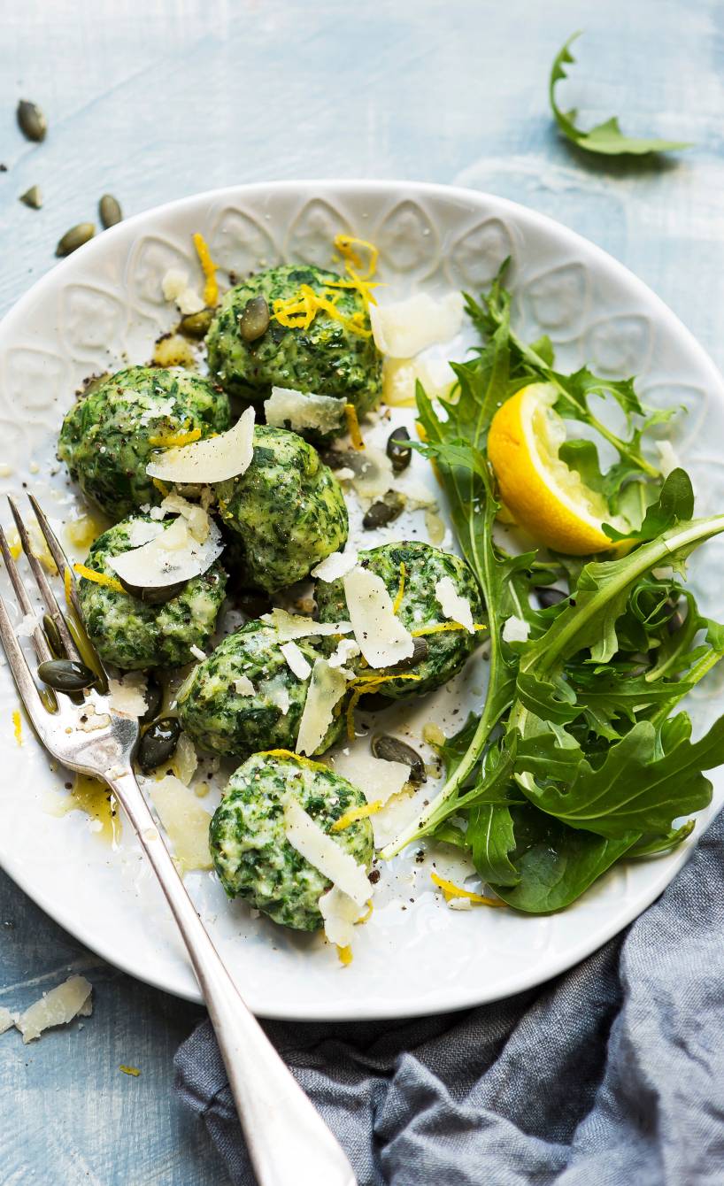 Selbstgemachte Spinat-Ricotta-Gnudi angerichtet auf Rucola mit Kürbiskernen und Parmesan auf einem Teller