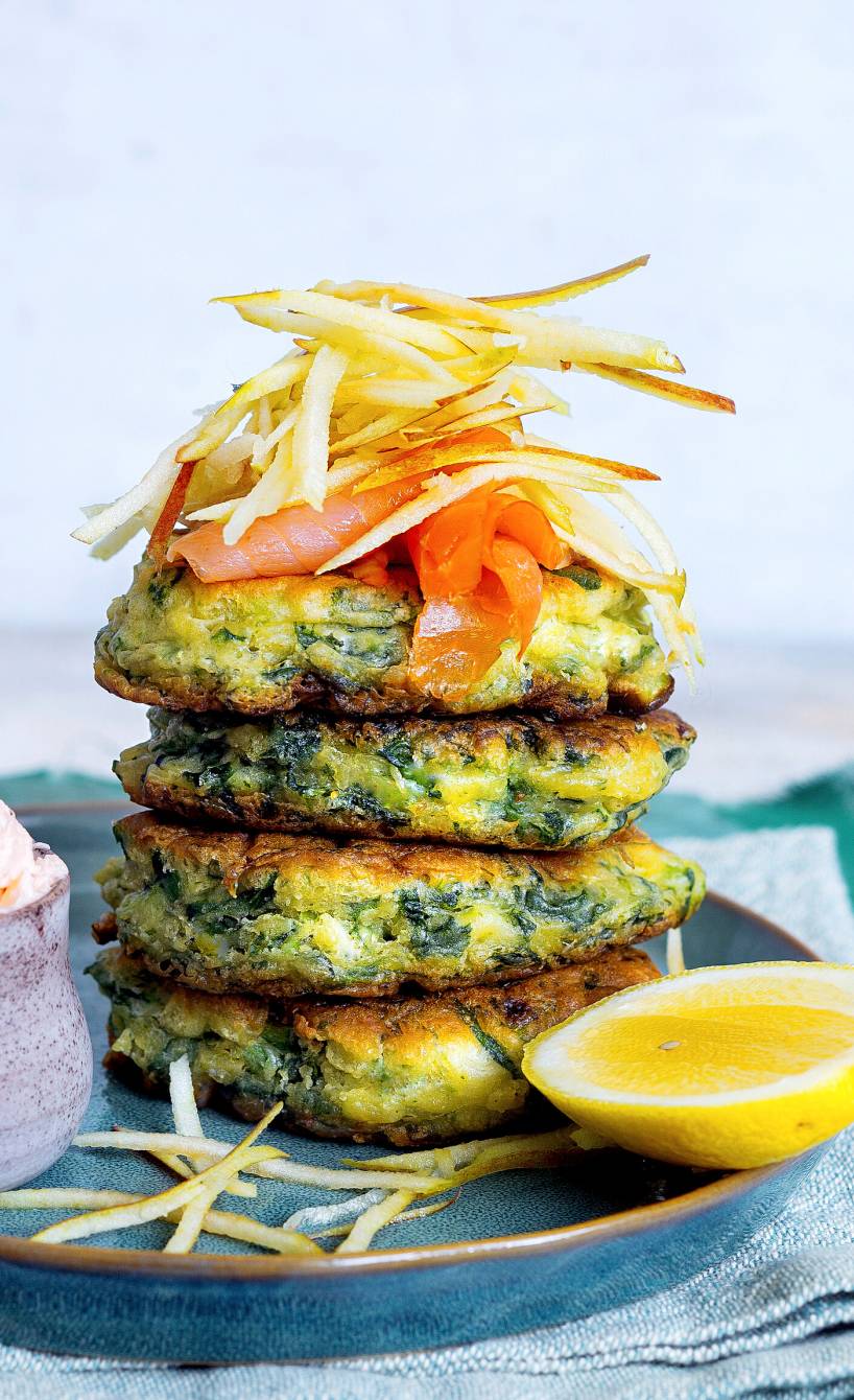 Vier Spinatpuffer gestapelt auf einem Teller, getoppt mit mit Räucherlachs