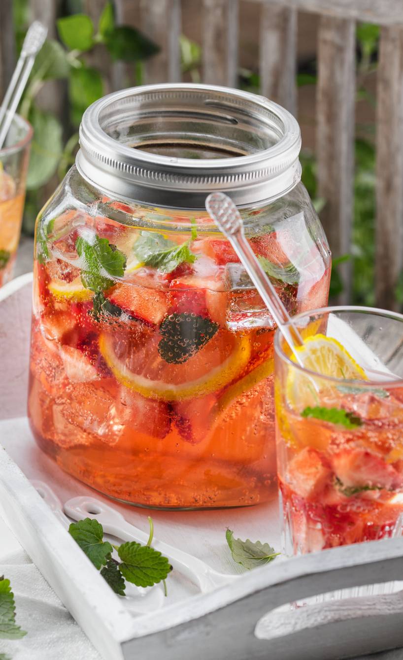 Selbstgemachte Erdbeerbowle in einem Bowleglas, daneben zwei Trinkgläser gefüllt auf einem Gartentisch