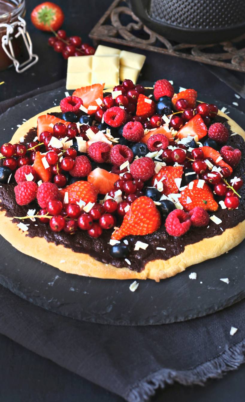 Süße Schokopizza mit frischen Beeren und weißen Schokoladenraspeln getoppt auf einer Schieferplatte