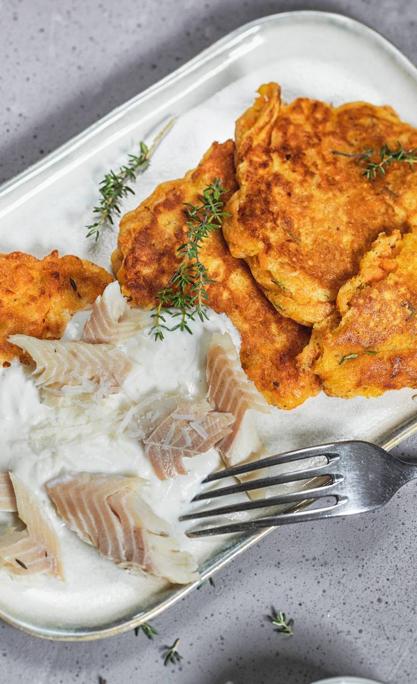 Süßkartoffel- Pfannkuchen auf einem Teller getoppt mit Parmesancreme, darauf Forellenfiletstücke