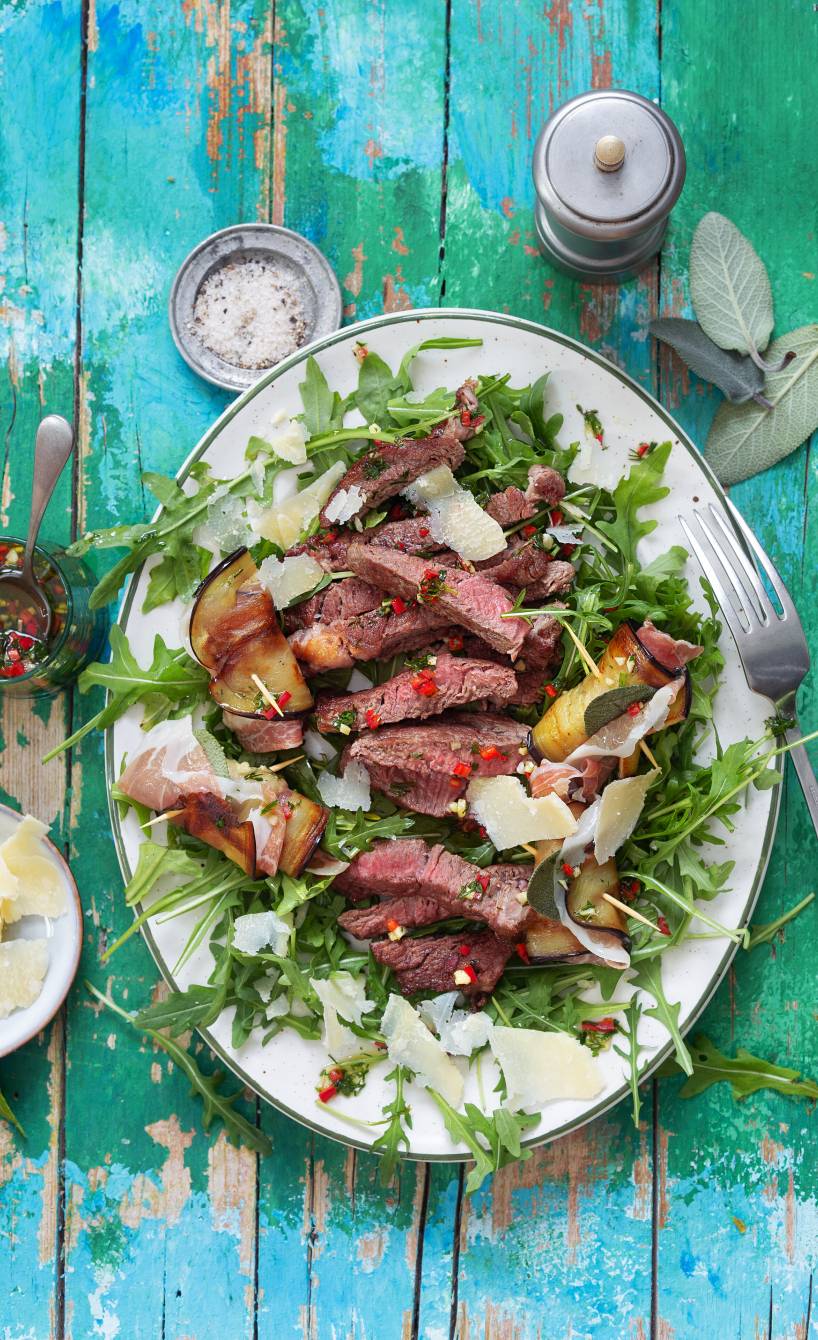 Teller mit Rindfleischstreifen und Auberginenröllchen auf einem Salatbett