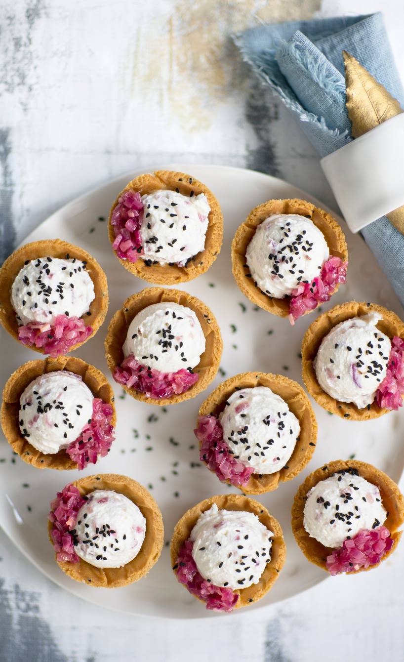 Tartelettes mit Käsecreme-Füllung getoppt von roten karamellisierten Zwiebeln und schwarzem Sesam auf einer Servierplatte