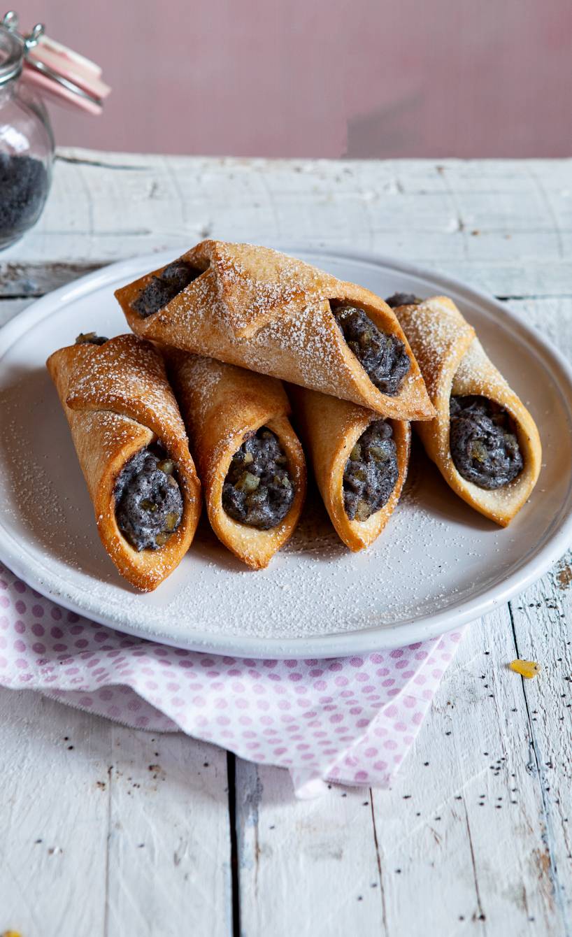 Fünf selbstgebackene Cannoli mit Mohn-Ricotta-Füllung gestapelt auf einem Dessertteller