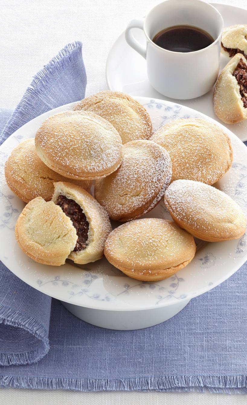 Bocconotti alle mandorle e cacao Teigtaschen mit Mandel-Kakao-Füllung auf einer Platte, schokoladige Füllung gut sichtbar, daneben eine Tasse Kaffee
