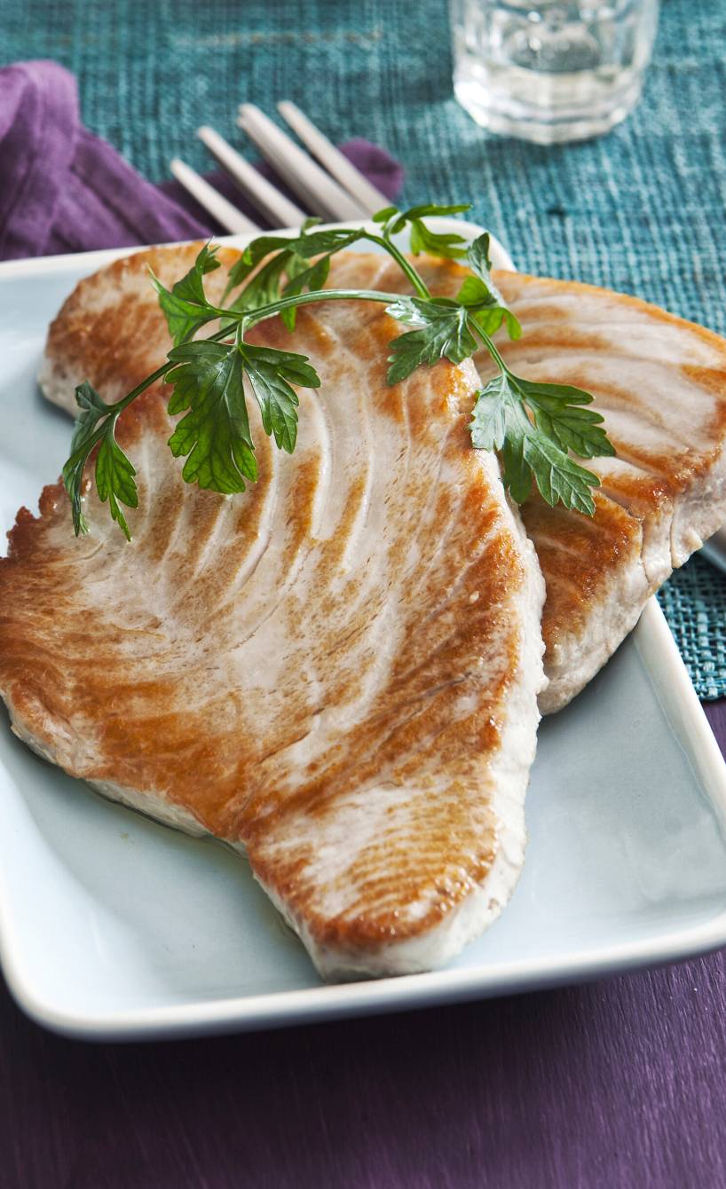 Zwei gebratene Thunfischsteaks auf einem rechteckigen Teller, daneben eine Schale mit rotem Pesto