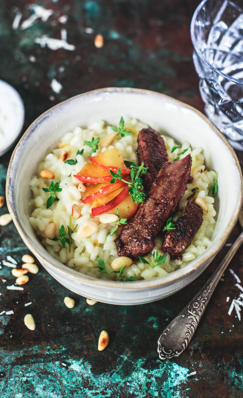 Drei Stücke gebratene Kalbsleber angerichtet auf Thymian-Apfel-Risotto auf einem tiefen Teller