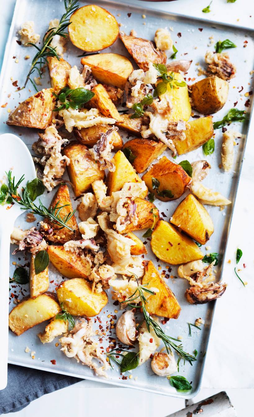 Tintenfisch und Kartoffeln aus dem Ofen auf einem Backblech, daneben ein Teller und eine Wasserflasche