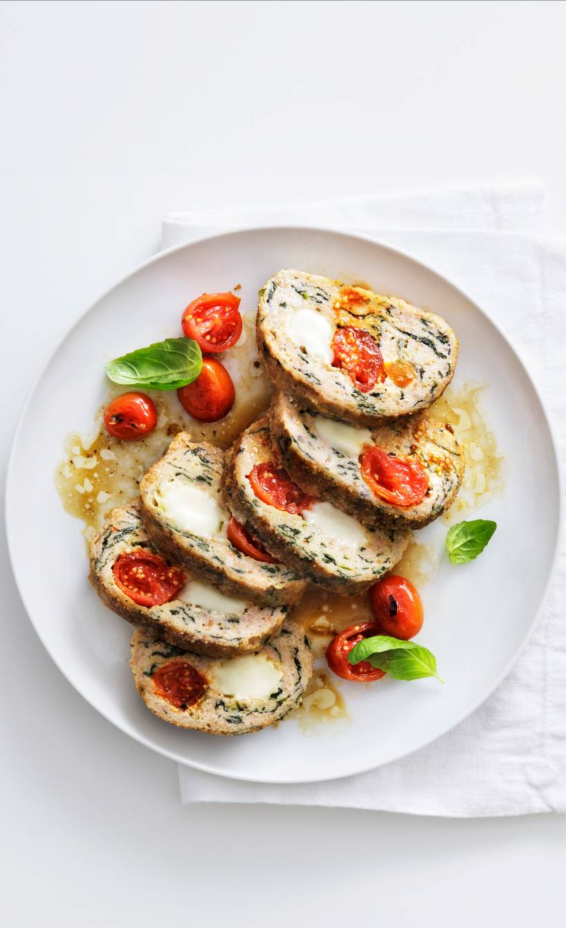 Mehrere Scheiben von gebackenem Putenhackbraten mit Tomaten-Mozzarella-Füllung angerichtet auf einer Servierplatte