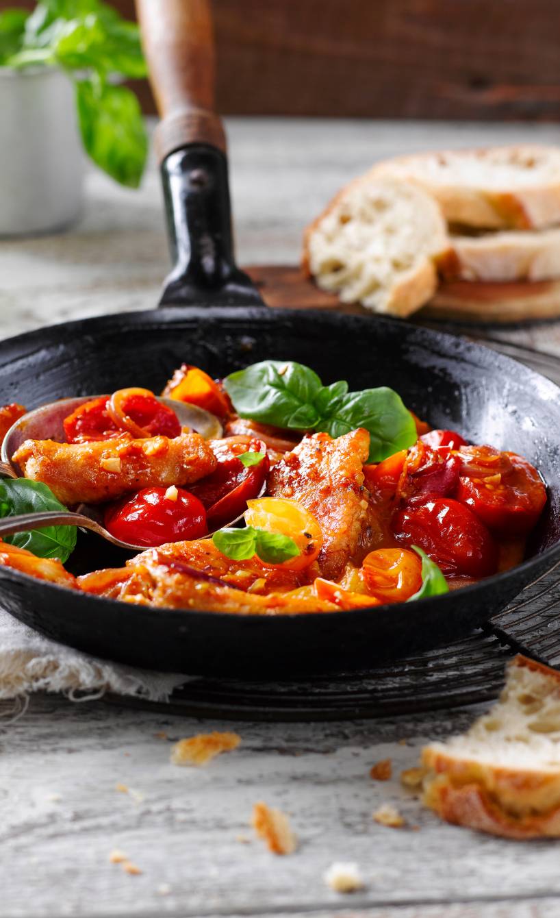 Pfanne mit Hähnchen und Tomaten auf einem Tisch, dekoriert mit Basilikum