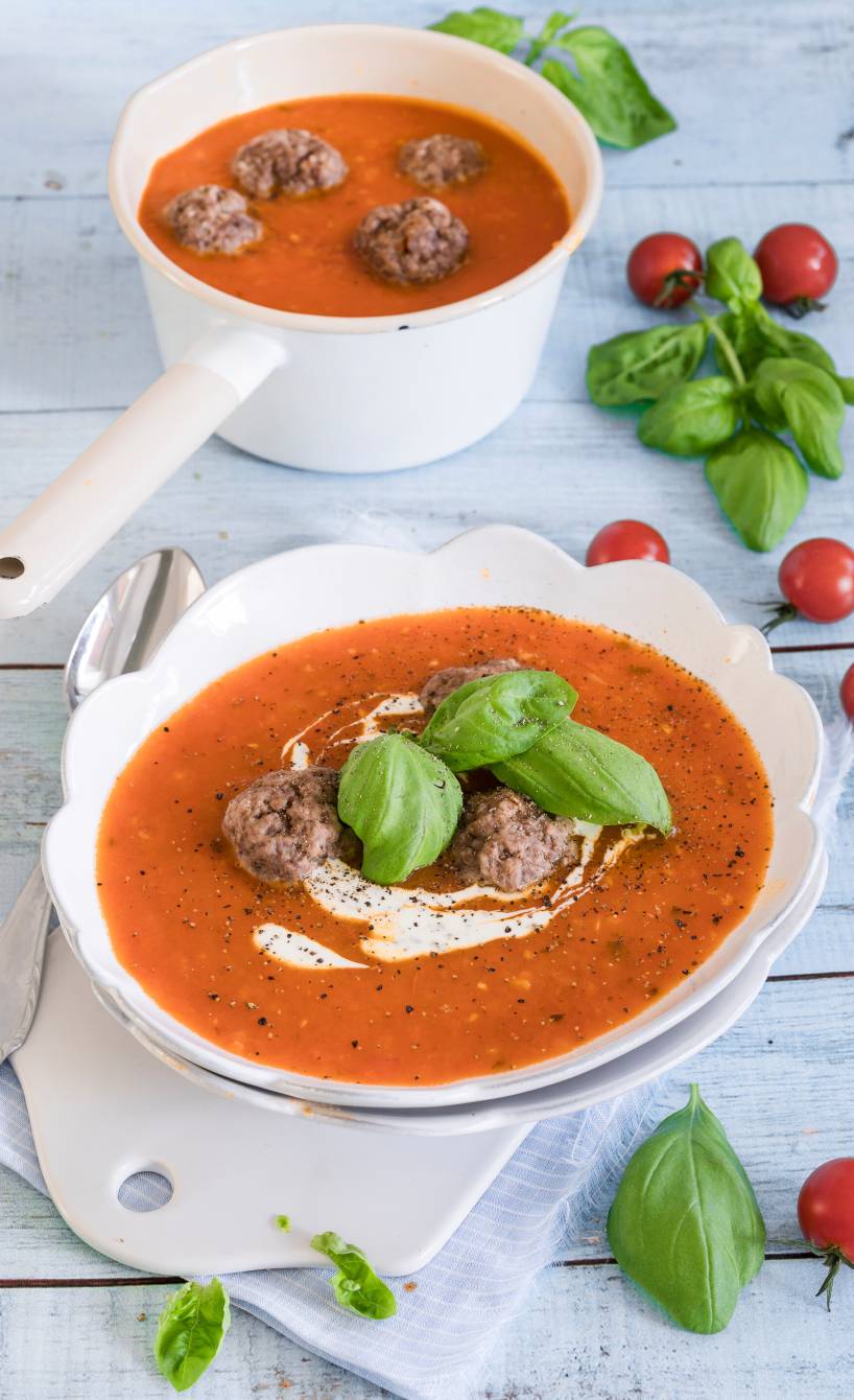 Italienische Tomatensuppe und einem Topf und in einem Suppenteller getoppt mit Hackbällchen, Crème fraîche und Basilikum