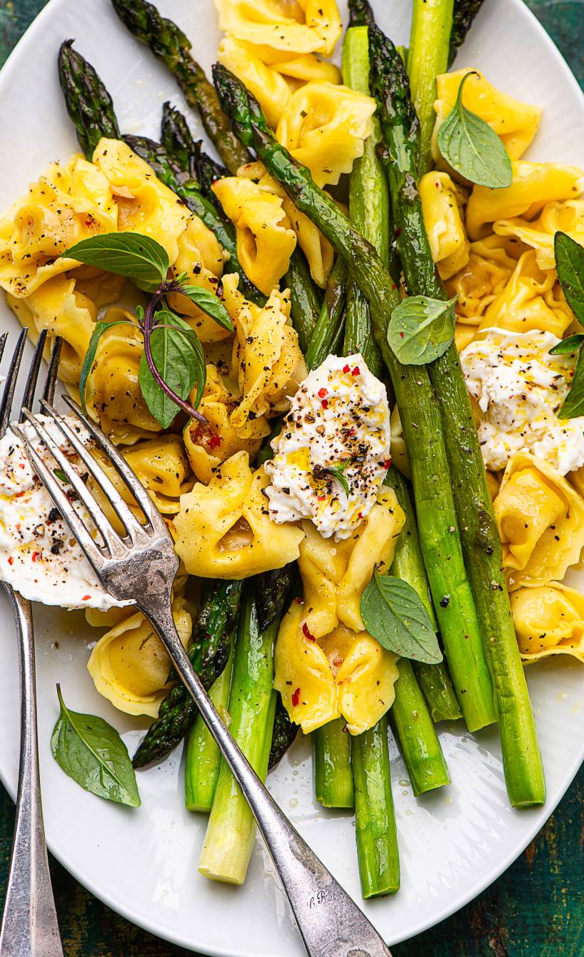 Tortellini auf einem ovalen Teller mit grünem Spargel getoppt von zerteiltem Burrata