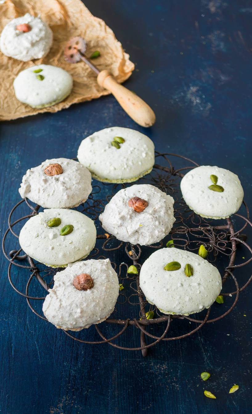 Zwei Sorten Weihnachtsplätzchen Haselnussplätzchen und Pistazien-Plätzchen auf einem Kuchengitter, daneben Weihnachtsdeko auf einem Tisch