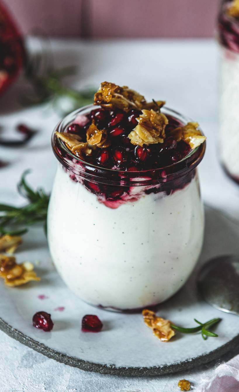 Vanillecreme in Gläsern getoppt mit Granatapfelsoße und Mandelkkrokant auf einem Tisch