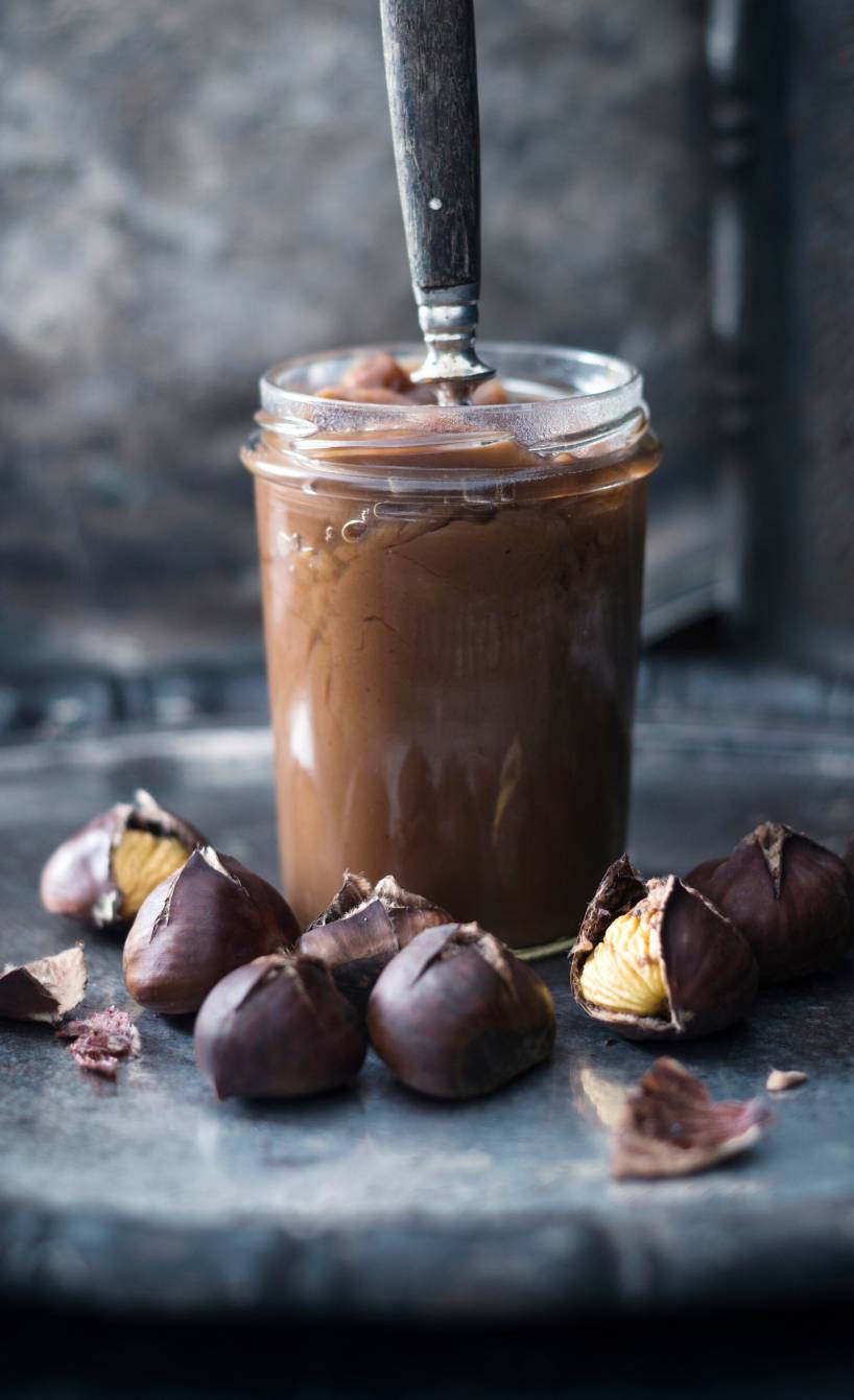 Selbstgemachter veganer süßer Maronenaufstrich in einem Weckglas auf eniem Tisch, daneben geröstete Maronen