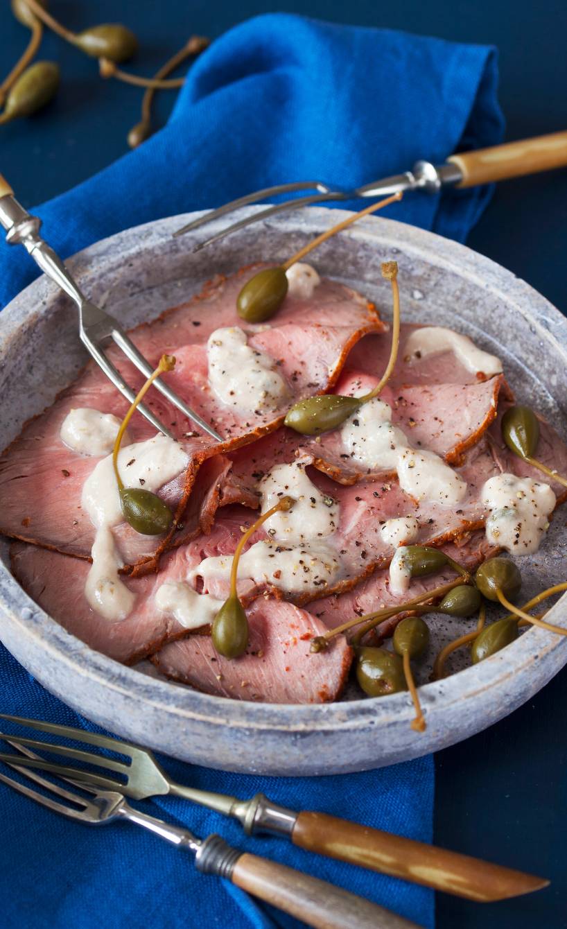 Vitello Tonnato aus Roastbeefscheiben angerichtet mit Kapernäpfeln und Thunfischsoße auf einem Vorspeisenteller