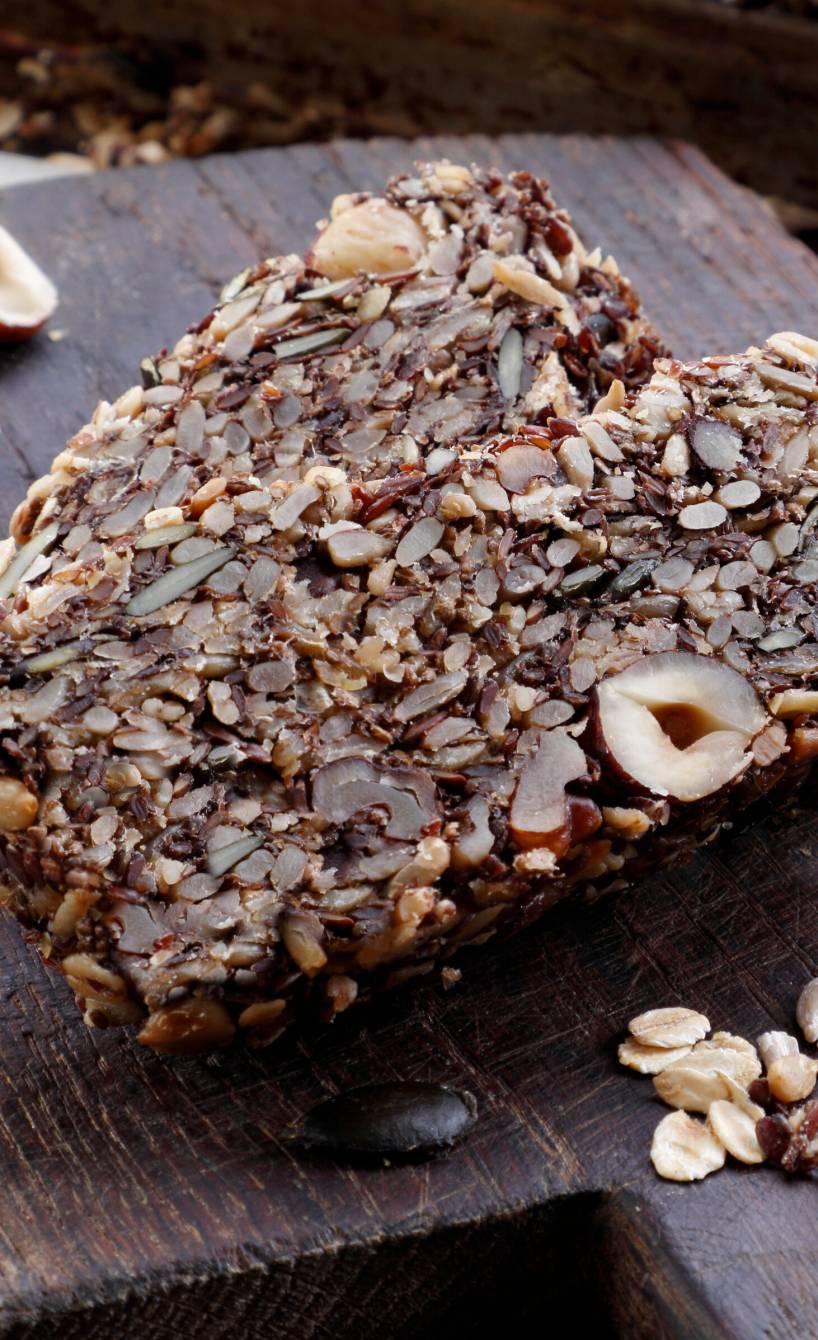 Vollkornbrot in Scheiben auf einem Holzbrett, daneben Nüsse