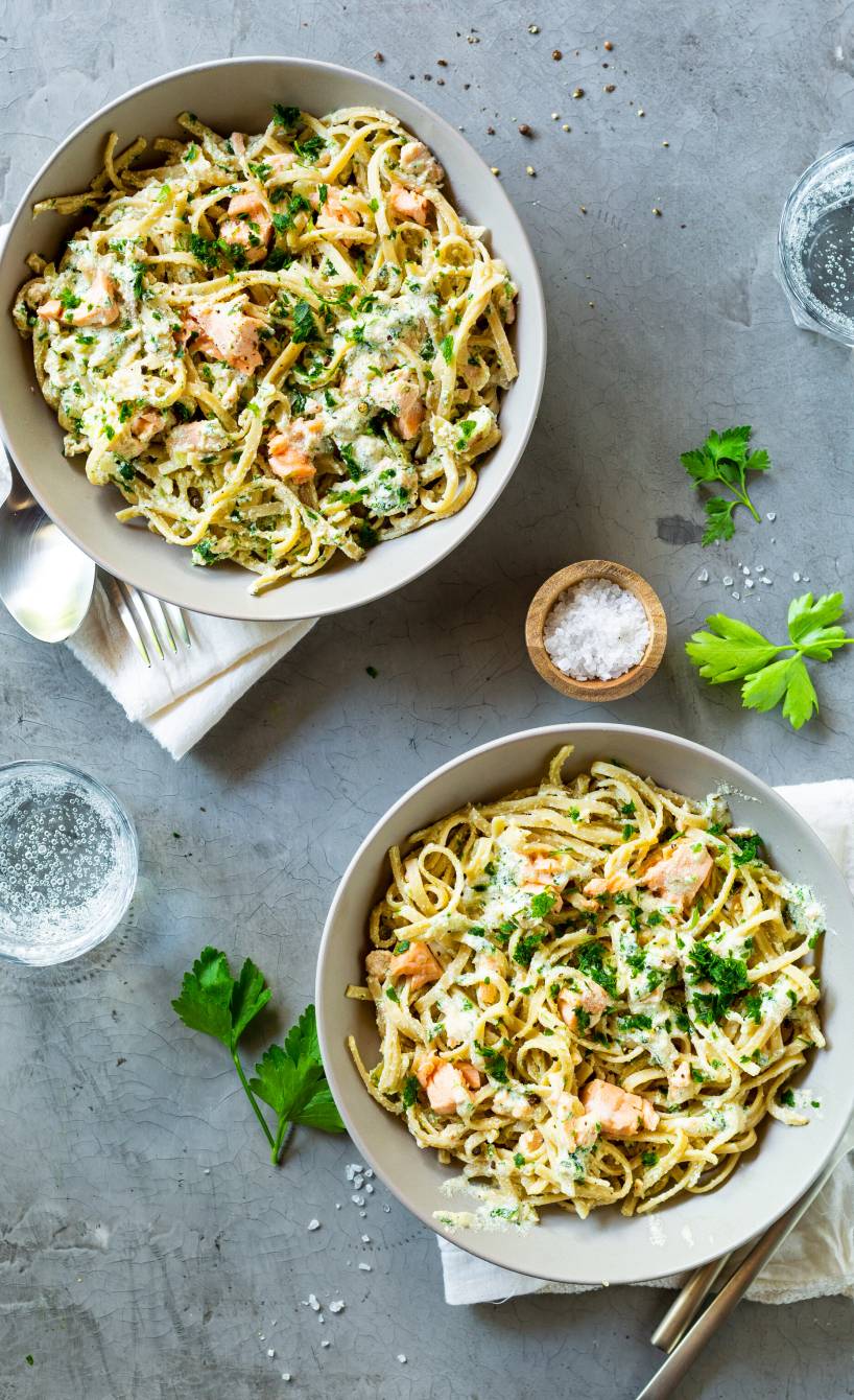 Vollkornnudeln mit Lachs und cremiger Sauce getoppt von frischen Kräutern in einem tiefen Teller