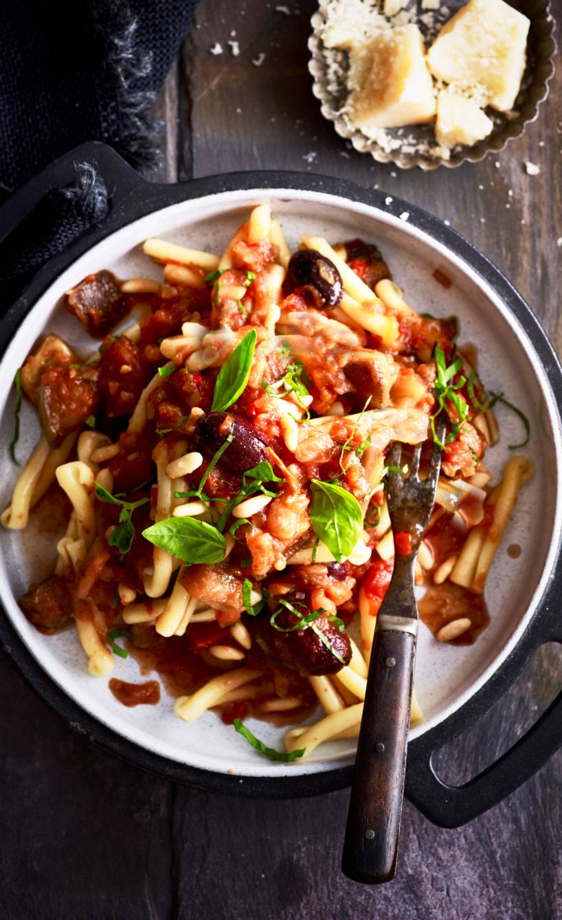 Vollkorn-Dinkelnudeln mit Sauce, Auberginen, Oliven und Pinienkernen angerichtet auf einem Teller