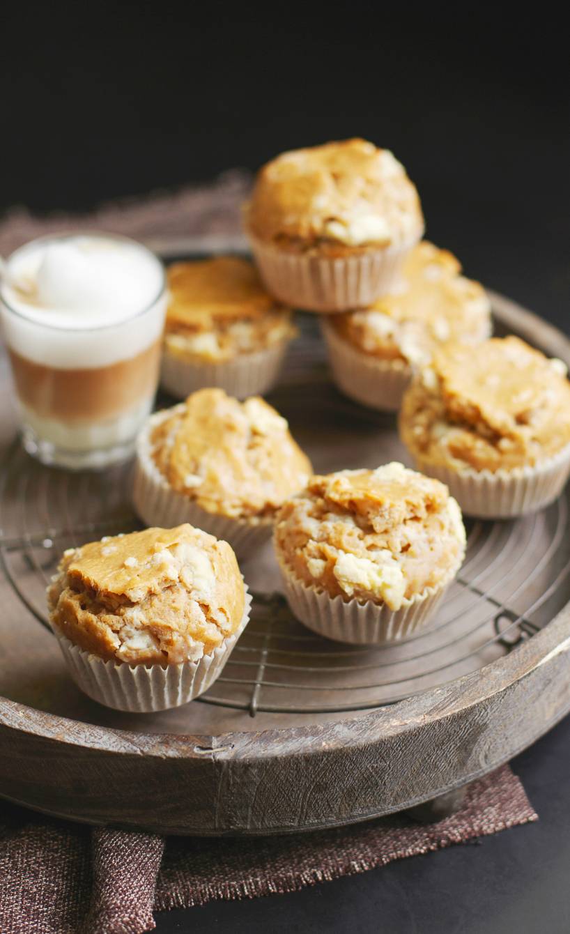 Sieben selbstgebackene Latte Macchiatto-Muffins auf einem Holztablett, daneben zwei Kaffeespezialitäten