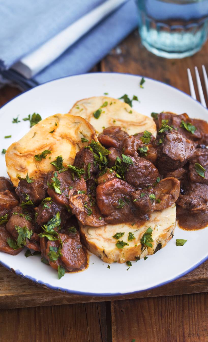 Wildgulasch mit Pilzen auf Serviettenknödeln auf einem Teller