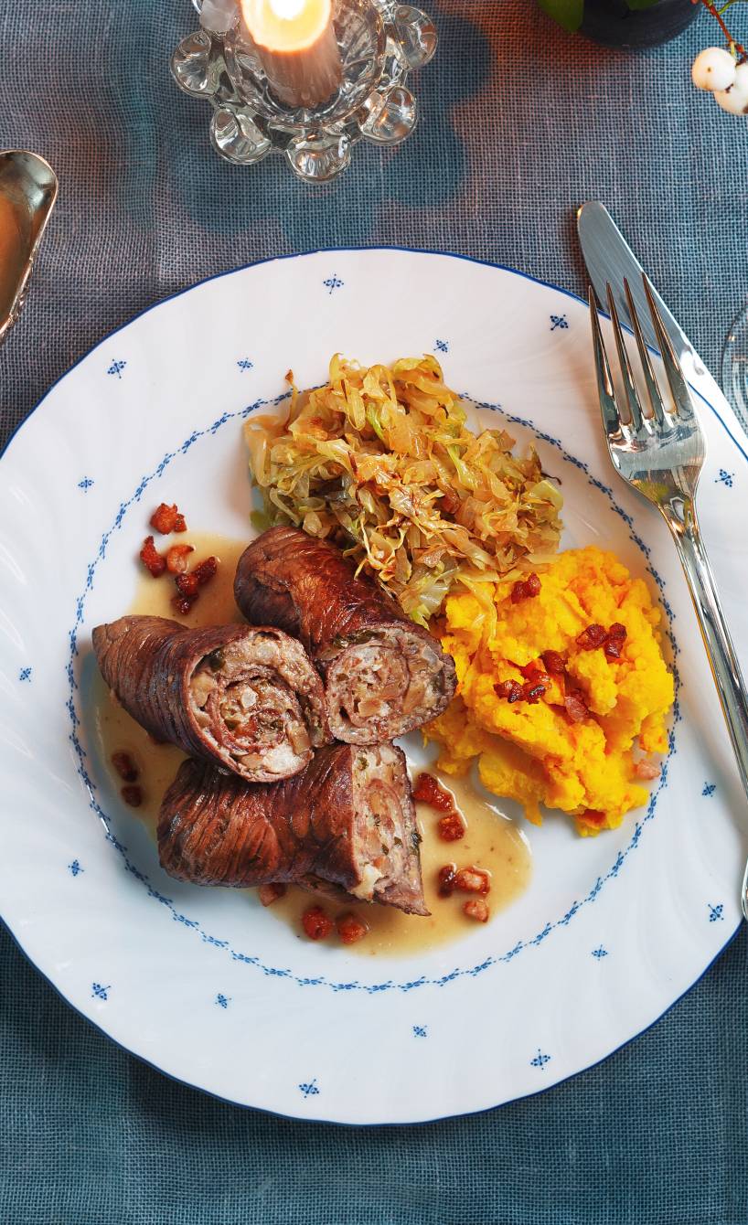 Wildschweinrouladen auf einem Teller, daneben Kürbis-Kartoffel-Stampf auf einem weihnachtlich dekorierten Tisch