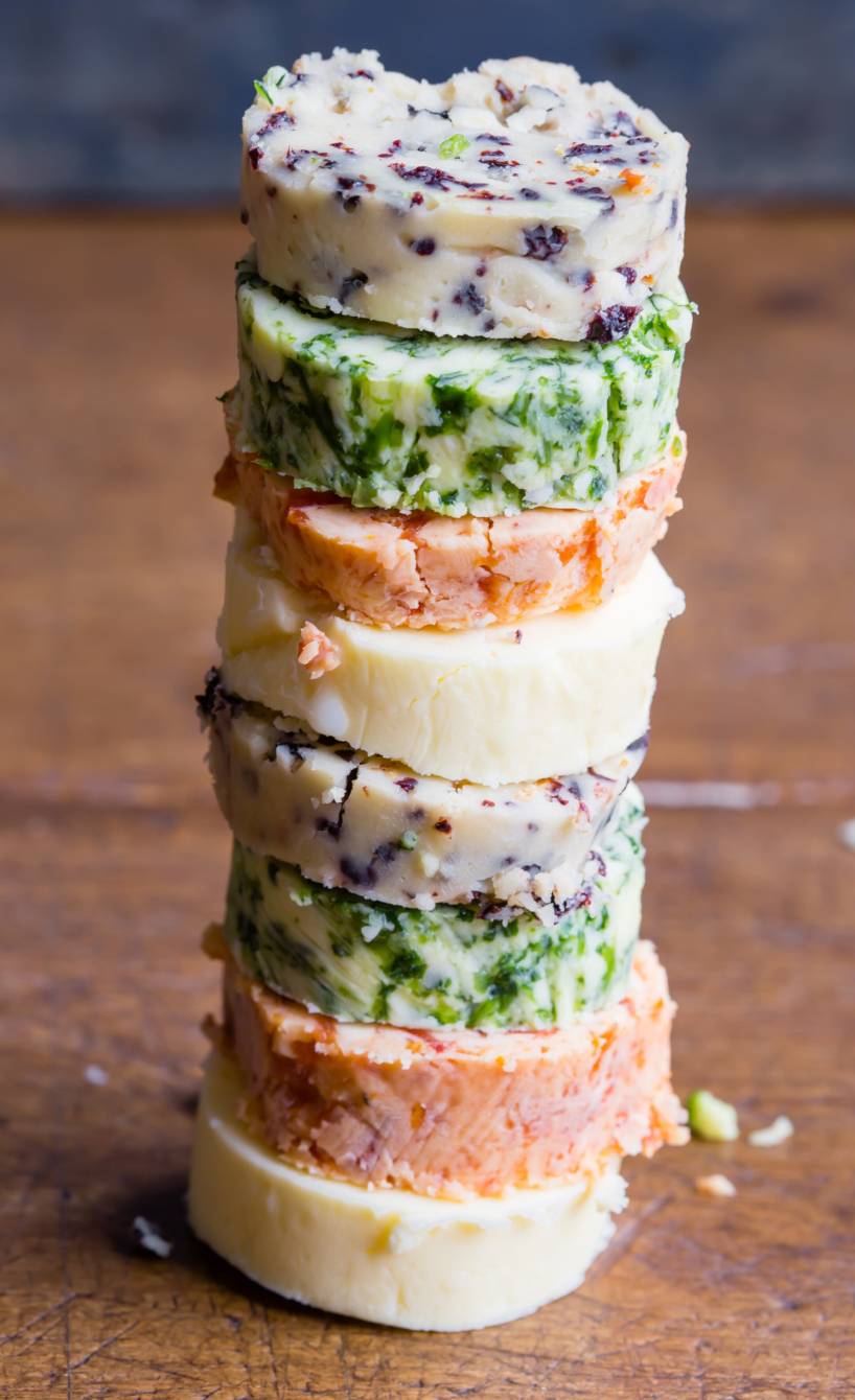 Verschiedene Stücke selbstgemachter Würzbutter-Rollen gestapelt auf einem Holzbrett