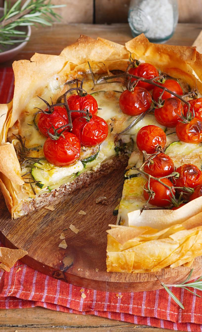 Hackfleisch-Quiche garniert mit Tomaten angeschnitten auf einem Tisch